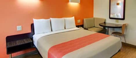 A hotel room with a bed, a desk, a chair, and a small table.