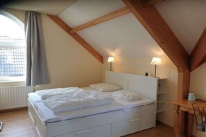 A bedroom with a white bed, two bedside lamps, a wooden table, and a window with curtains. - Holiday paradise sea air (Kamperland)