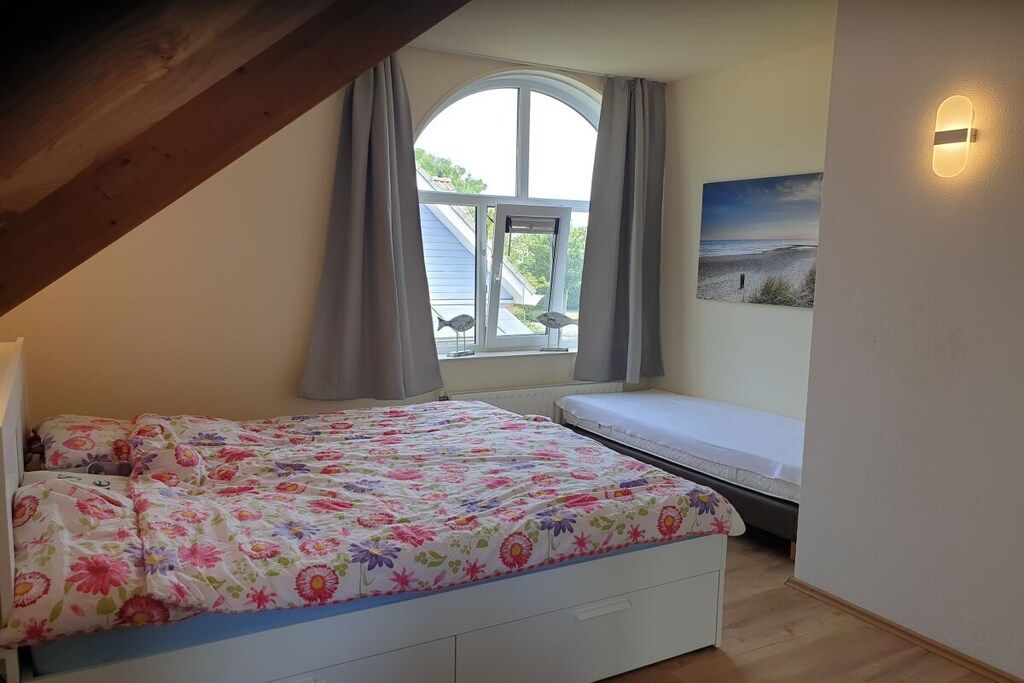 Une chambre à coucher avec un lit, une fenêtre avec des rideaux, un luminaire fixé au mur et un tableau sur le thème de la plage.
