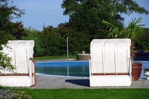 Two wicker lounge chairs by a swimming pool with a hedge and trees in the background. - Holiday apartment Rügen (Sagard - Neddesitz)