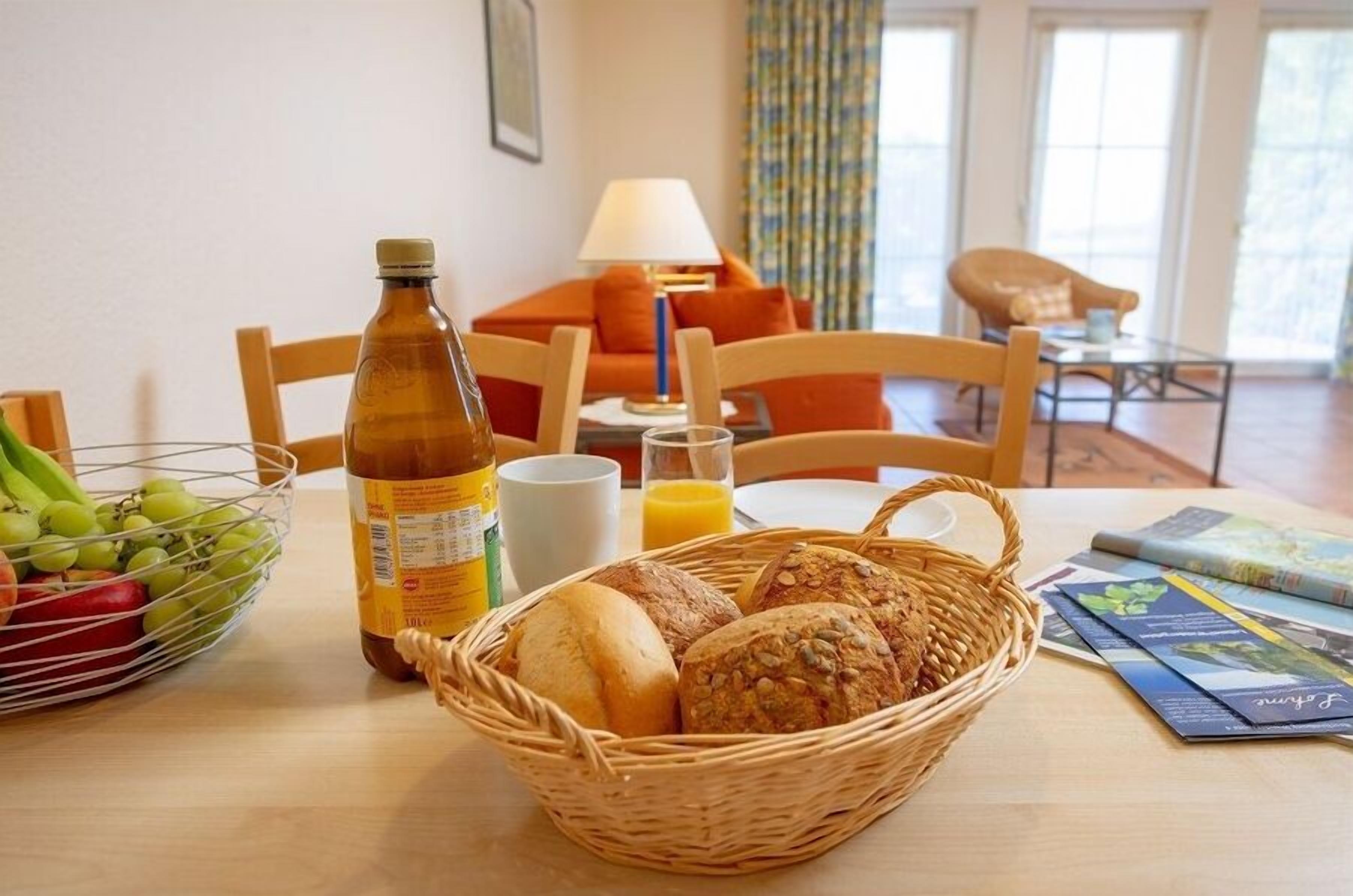 A breakfast setting with bread, a bottle, and a fruit bowl on a table.