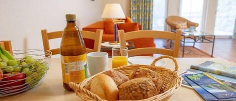 A breakfast setting with bread, a bottle, and a fruit bowl on a table.