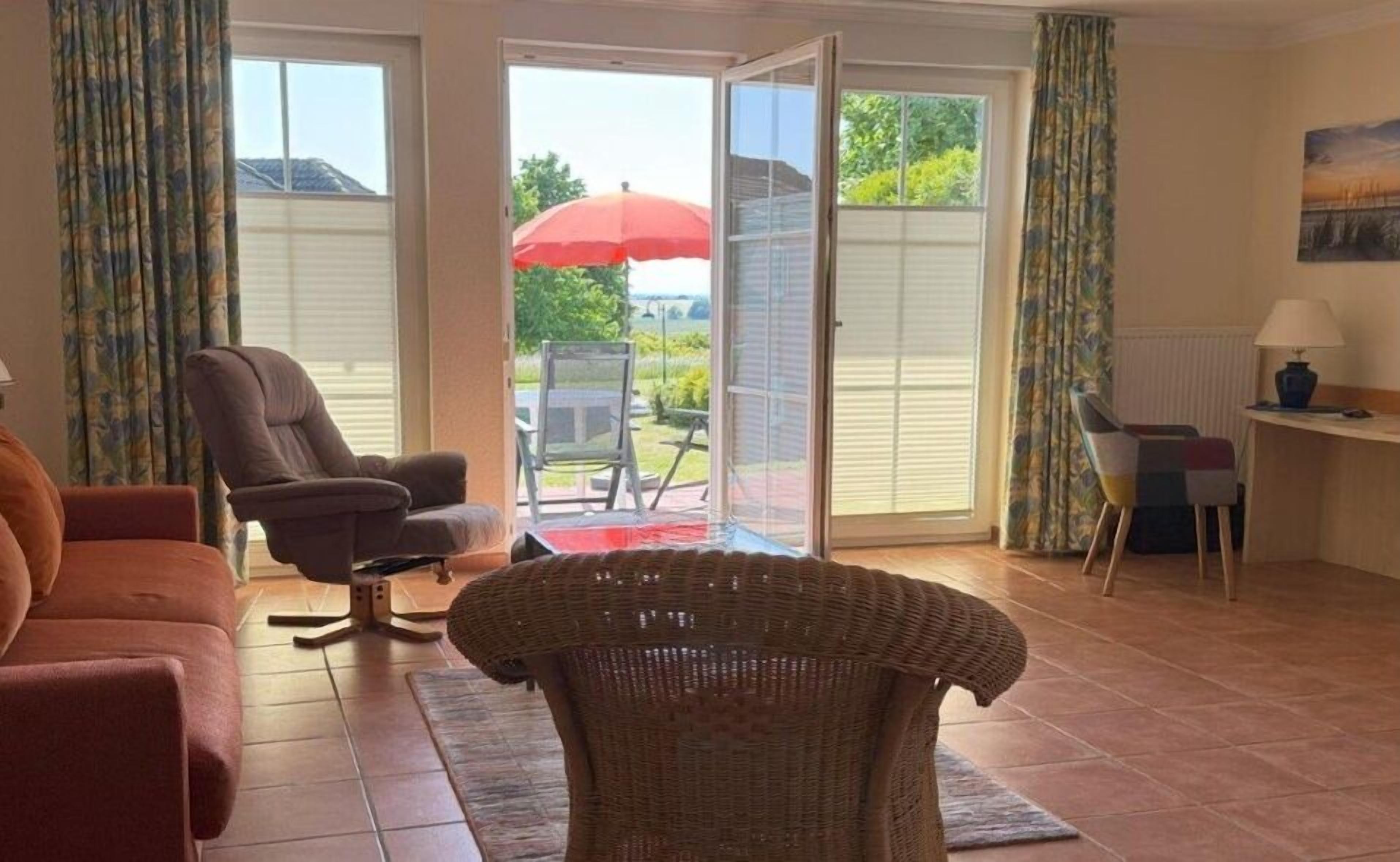 Un salon avec un canapé, un fauteuil et une chaise en osier. On y trouve une table avec une lampe et un tableau accroché au mur.