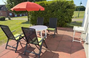 An outdoor patio with a round table and four chairs, a red umbrella, and a white table. - Holiday apartment Rügen (Sagard - Neddesitz)