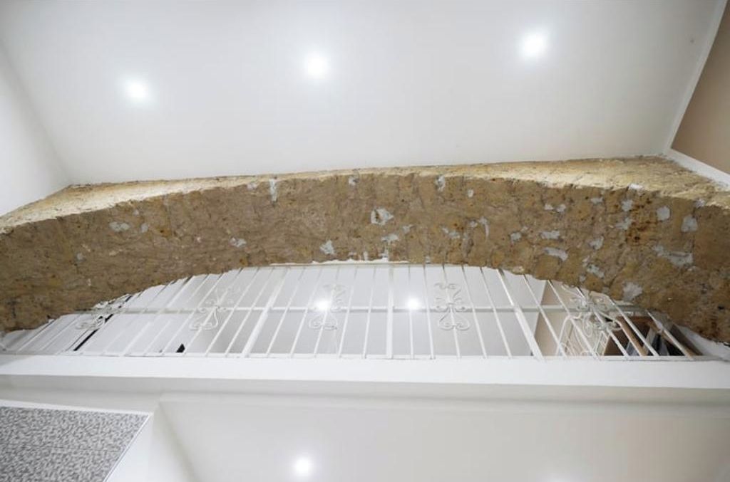 A room with a white ceiling, a white wall, and a white floor. There is a white railing in the corner.