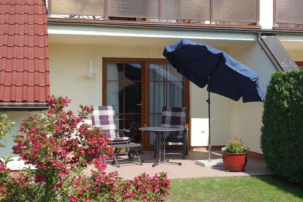 En terrasse med et bord, stole, en potteplante og en stor parasol.