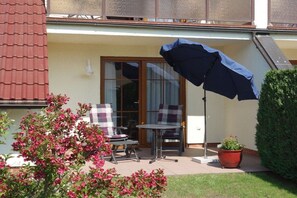 Eine Terrasse mit Tisch, Stühlen, einem Blumentopf und einem großen Sonnenschirm.