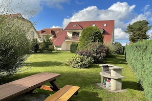 Ein Wohnhaus mit gepflegtem Rasen, einem Picknicktisch und einer Grillgelegenheit.