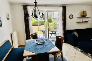 Een eetruimte met een tafel, stoelen, een kroonluchter en uitzicht door glazen deuren op een buitengebied.