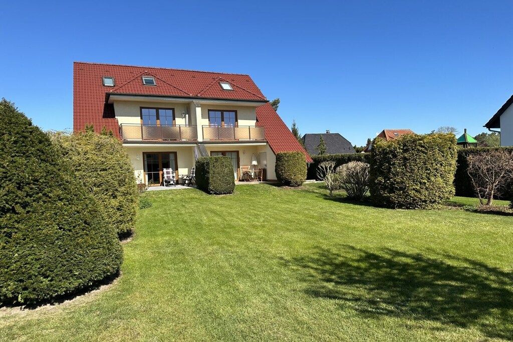 Une maison à deux étages avec un toit rouge, un balcon au deuxième étage et une pelouse bien entretenue.