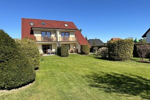 Ein zweistöckiges Haus mit rotem Dach, einem Balkon im zweiten Stock und einem gepflegten Rasen.