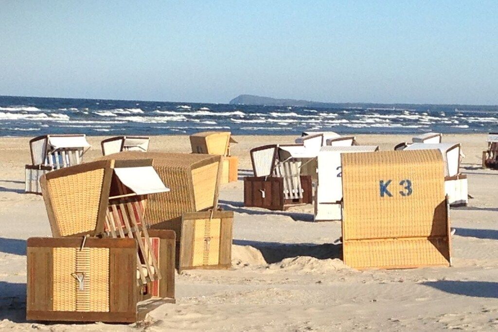 Strandstühle und eine Holzkonstruktion mit der Aufschrift 'K3' an einem Sandstrand, im Hintergrund das Meer.