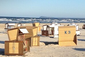Strandstoelen en een houten constructie met de aanduiding 'K3' op een zandstrand, met de oceaan op de achtergrond.