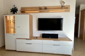 Ein modernes Wohnzimmer mit einem an der Wand befestigten Flachbildfernseher, einer Holzunterhaltungseinheit darunter und einer Vitrine mit Glastüren.