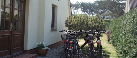 Un bâtiment doté d’une porte et de fenêtres, une zone pavée avec des vélos et une haie.
