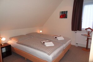 Un lit simple avec une couvre-lit à carreaux et des oreillers, une lampe de chevet, un radiateur et une fenêtre avec des rideaux.