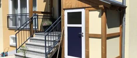 A two-story building with a wooden porch, a staircase, and a door.
