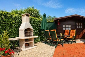 Eine Terrasse im Freien mit einem gemauerten Pizzaofen, einem runden Tisch und grünen Stühlen.