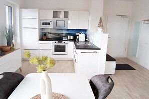 A modern kitchen with white cabinetry, a black countertop, and a dining area with a white table and two chairs. - Holiday apartment in Glowe with swimming pool (Glowe)
