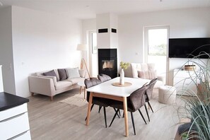 A modern living room with a fireplace, a dining table, and a sofa. - Holiday apartment in Glowe with swimming pool (Glowe)