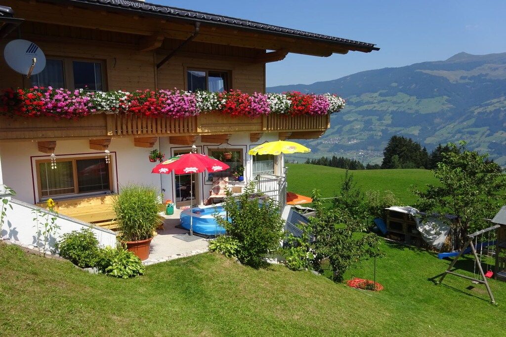 Una cabaña con balcón decorado con flores, piscina y vistas a las montañas.