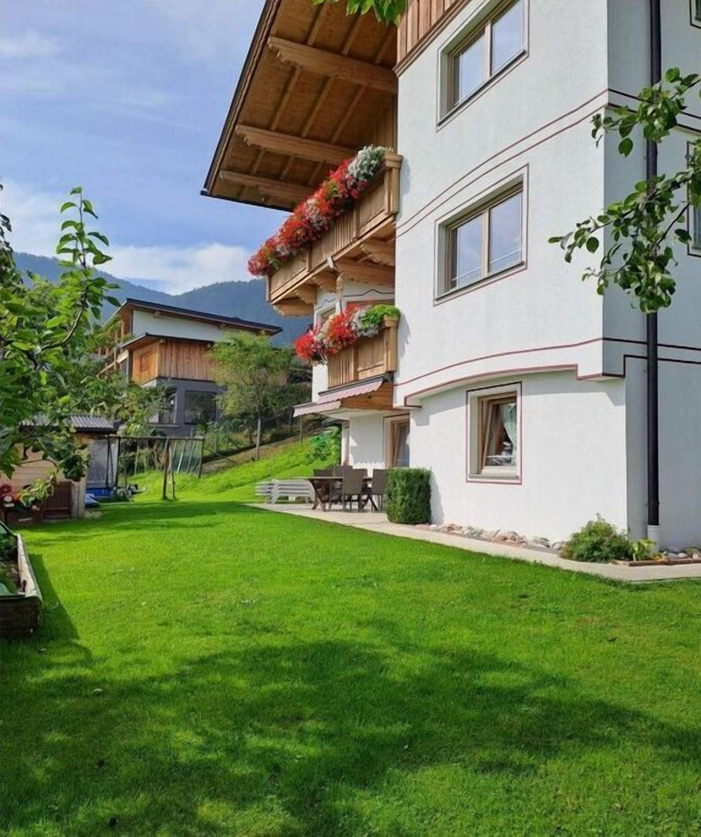 A two-story building with balconies adorned with flowers, a well-maintained lawn, and a clear view of the surrounding landscape.