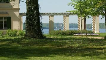 A garden with a pergola, a body of water, and a building with a balcony.
