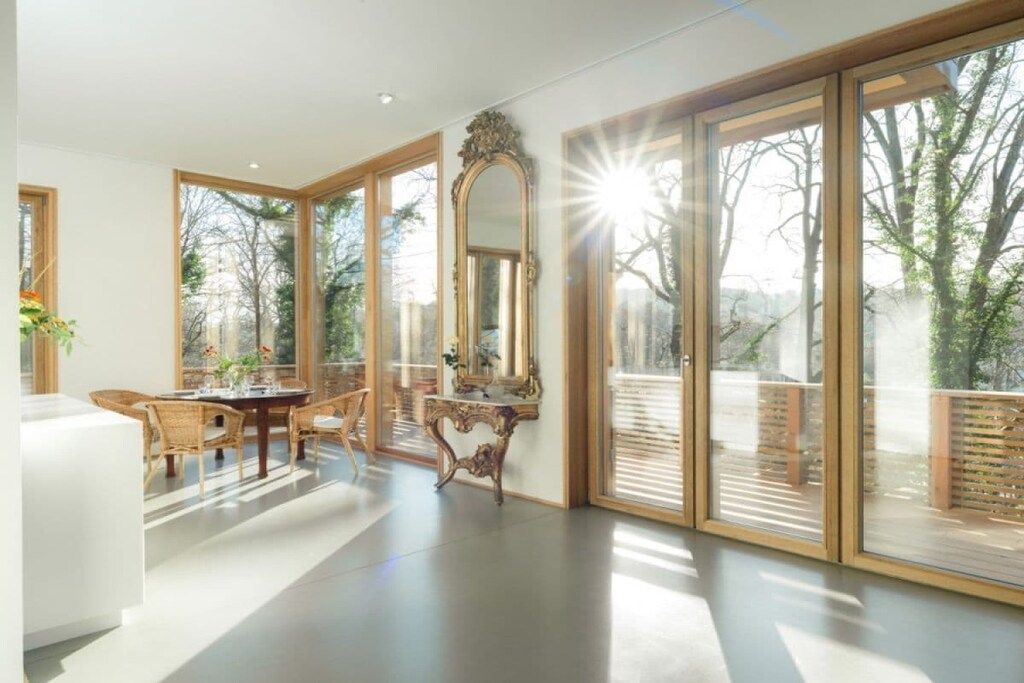 A spacious room with large windows, a dining area with wicker furniture, and a decorative mirror.