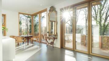 A spacious room with large windows, a dining area with wicker furniture, and a decorative mirror.