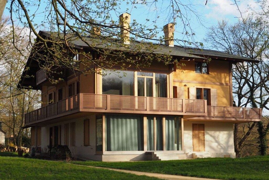 A two-story house with a balcony, large windows, and a chimney.
