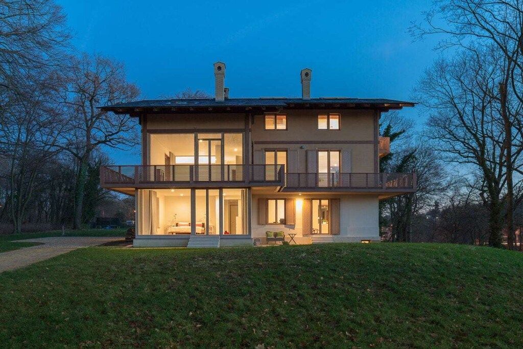 A two-story house with a balcony, large windows, and a well-maintained lawn.