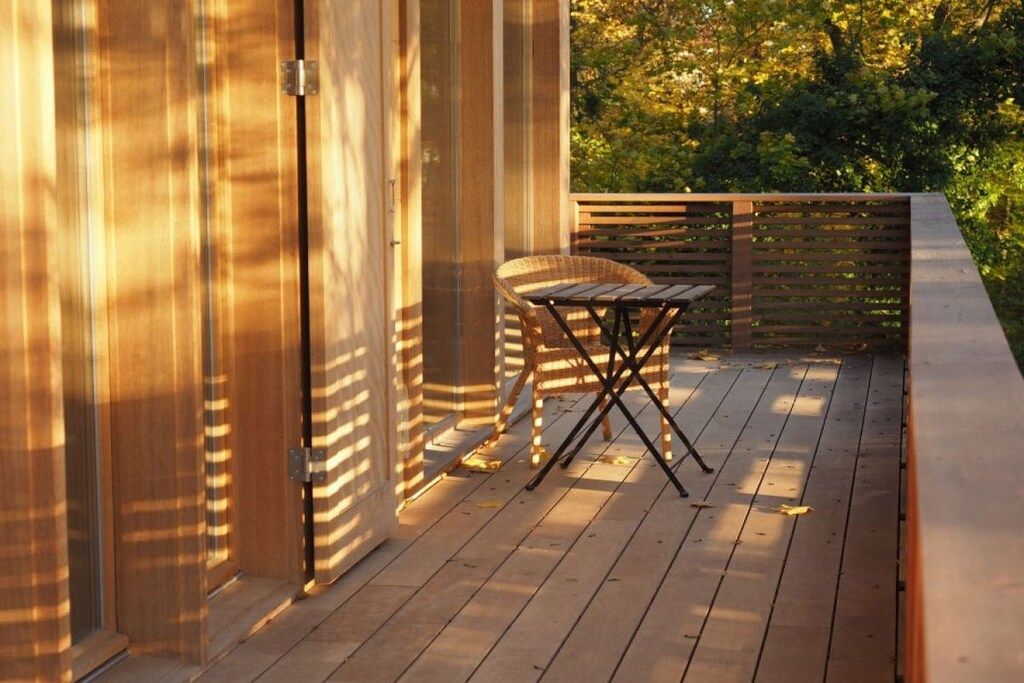 A wooden deck with a table and chairs, surrounded by wooden railings and a view of trees.