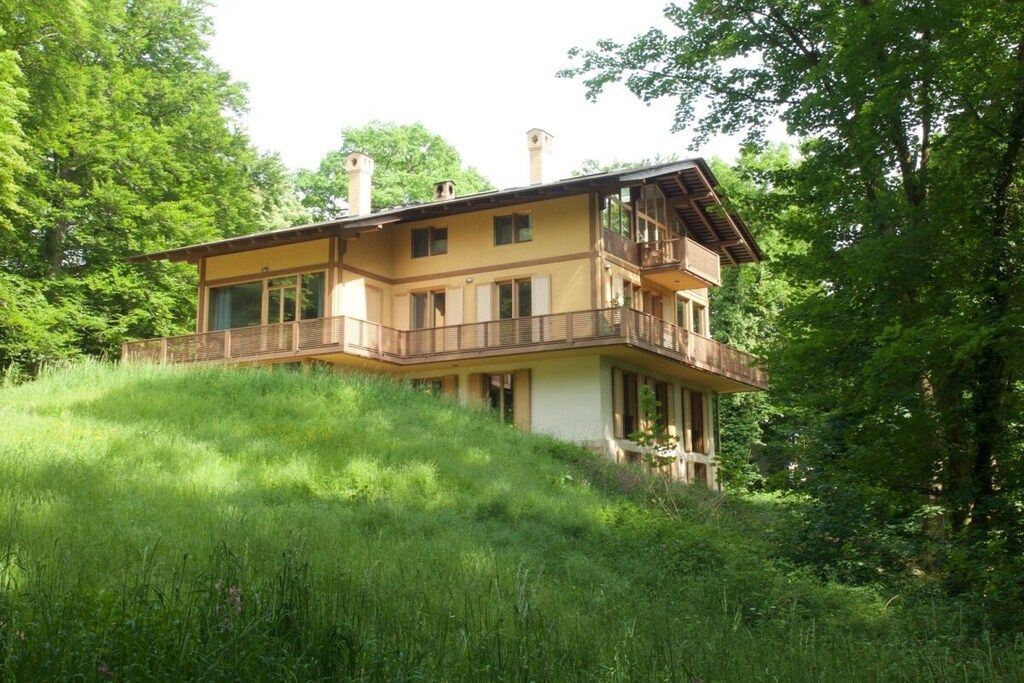 A two-story building with a balcony on the upper floor, surrounded by lush greenery.