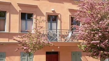 En bygning med balkon, rød dør og et blomstrende træ i forgrunden.