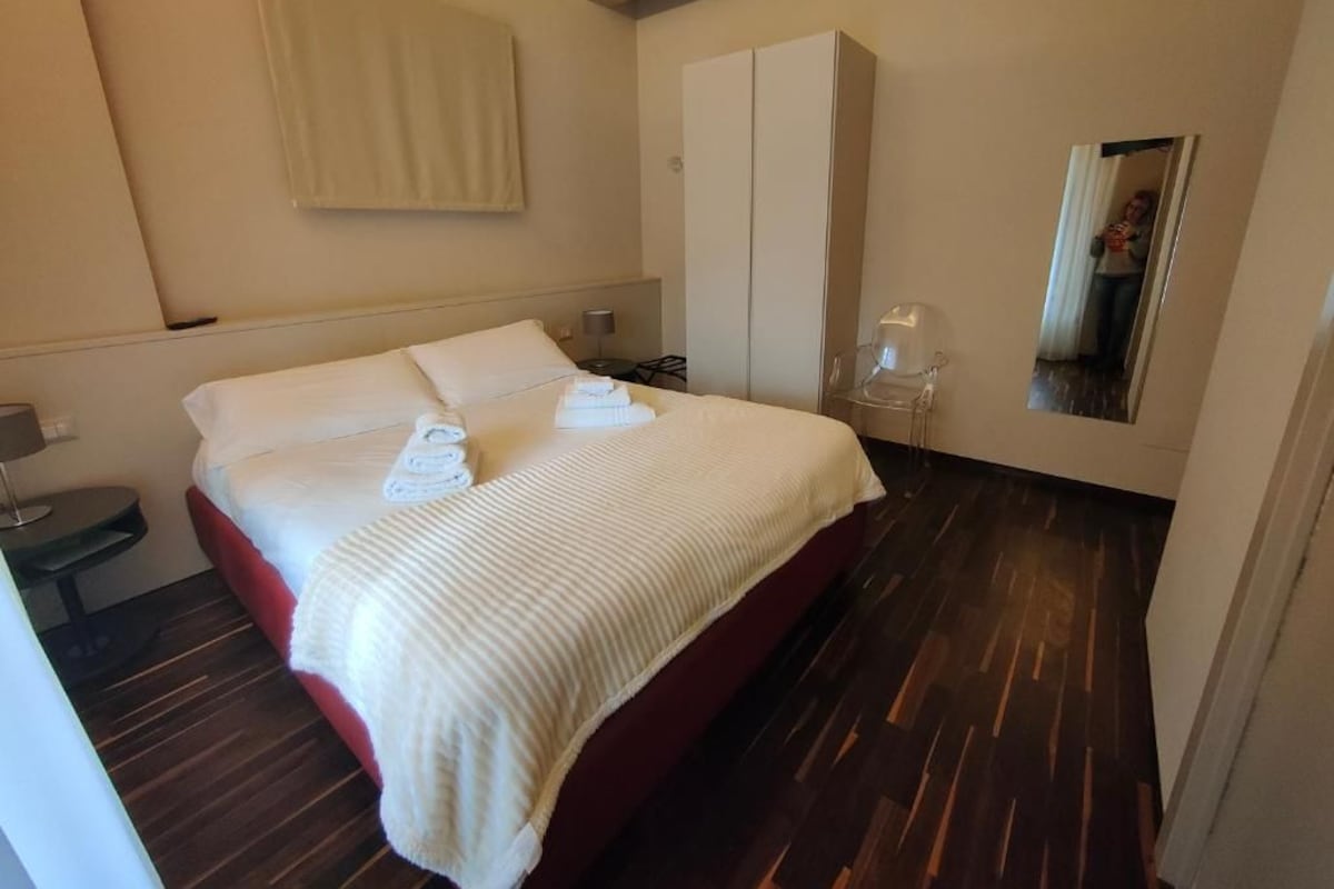 Quarto de hotel com cama, guarda-roupa, mesa de cabeceira e espelho.