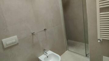Un baño con inodoro, bidé y ducha con mampara de vidrio.
