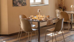 Een eethoek met een tafel voor twee personen, stoelen, een lamp en een schilderij aan de muur.