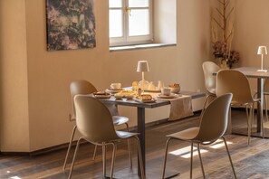 Uma área de refeições com mesa posta para dois, cadeiras, luminária e um quadro na parede.