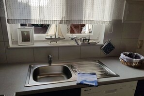 Eine Küche mit einem doppelten Spülbecken, einem Geschirrspüler und einem Fenster mit Vorhängen.