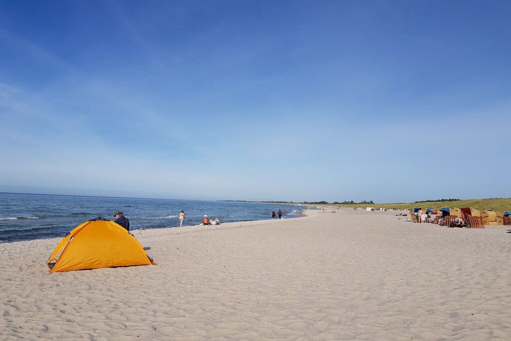 Een strand met een gele tent en strandstoelen.