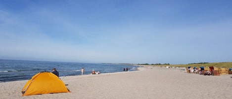 Una playa con una carpa amarilla y sillas de playa.
