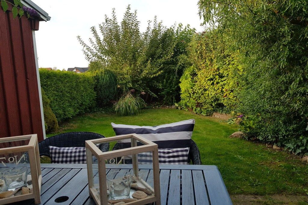Een terras met een tafel en stoelen, omgeven door groen en een haag.