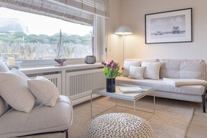 A living room with a sofa, a coffee table, a lamp, and a framed picture on the wall. - Friesenkoje in Mellhörn (List)