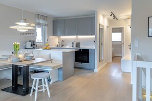 A modern kitchen with a central island, pendant lighting, and a view into the adjacent living area. - Friesenkoje in Mellhörn (List)