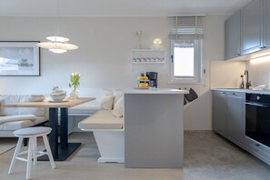 A modern kitchen with a central island, a dining area with a white table and chairs, and a built-in oven. - Friesenkoje in Mellhörn (List)
