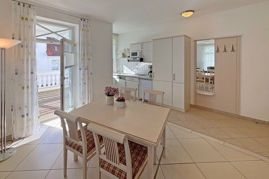 A modern kitchen with white cabinets, a dining area with a table and chairs, and a view through a glass door to an outdoor balcony.