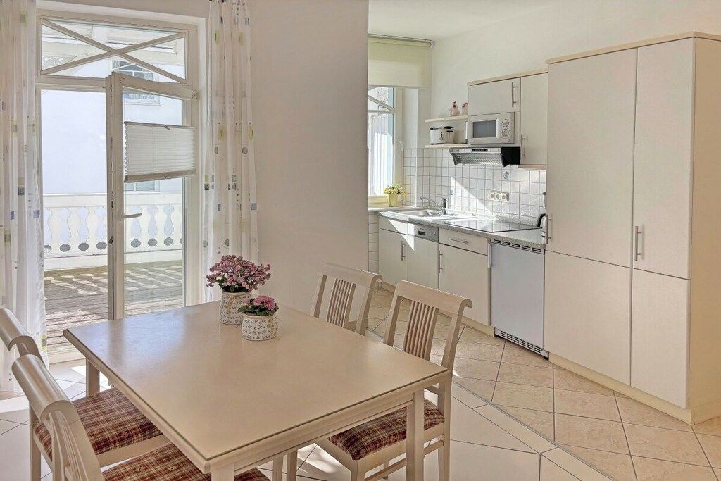 Un coin repas avec une table et des chaises, une cuisine avec des meubles blancs et une vue à travers une porte vitrée.