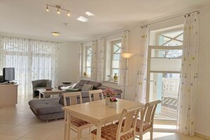 A modern living room with a dining area, large windows, and a balcony. - No. 9 in Villa Strandburg (Ostseebad Binz)
