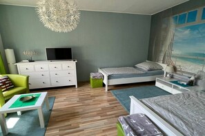 Ein Schlafzimmer mit einem Bett, einem Schreibtisch, einem Stuhl, einem Fernseher und einem Bild mit einer Strandansicht.