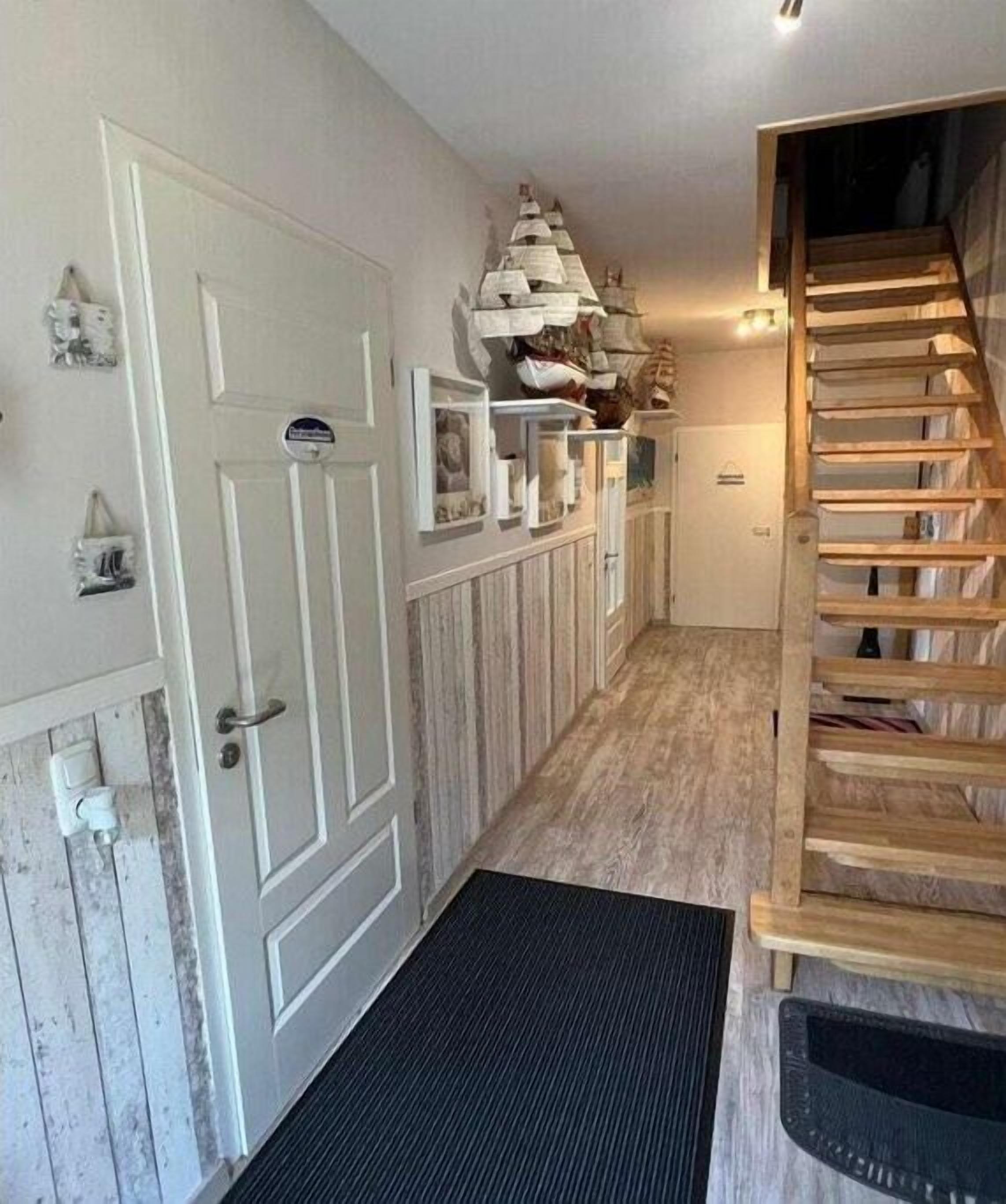 A hallway with a wooden staircase, a white door, and a shelf with decorative items.